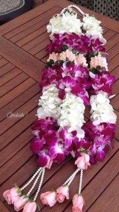 purple and white flowers are arranged on a wooden table with pearls hanging from the end