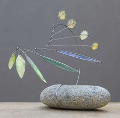 a metal sculpture sitting on top of a rock next to a leaf and flower decoration