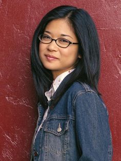 a woman wearing glasses leaning against a red wall