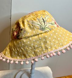 This bucket hat is made from polka dot cotton and patchwork with floral  cutouts that are stitched on.  Great for keeping the sun out in style!    Super cute pastel colors.   The hat measures 22-24 inches.  Embellished with pink ball fringe. Handmade Whimsical Sun Hat For Summer, Playful Summer Sun Hat For Festivals, Playful Handmade Sun Hat For Summer, Whimsical Adjustable Sun Hat For Summer, Whimsical Summer Beach Hats, Playful Reversible Summer Hat, Handmade Summer Sun Hat For Garden Party, Yellow Reversible Bucket Hat For Beach, Reversible Yellow Spring Hat