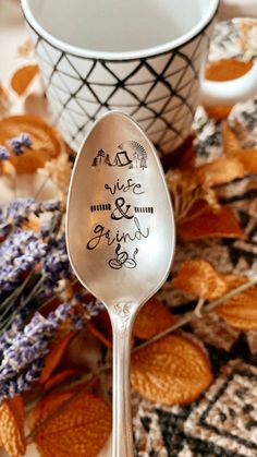 a silver spoon with writing on it sitting next to a cup and saucer filled with dried flowers