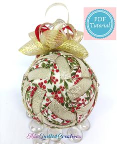 a christmas ball ornament with gold ribbon and holly leaves on it's side