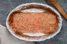 an uncooked meatloaf in foil with a wooden spoon on the side