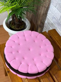 a pink round cake sitting on top of a wooden table next to a potted plant