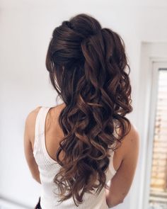 a woman with long brown hair is standing in front of a window and has her back turned to the camera