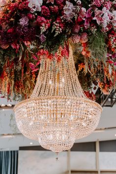 a chandelier hanging from the ceiling in front of a large flower arrangement with pink and red flowers