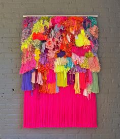 a colorful wall hanging on the side of a brick building with lots of tassels attached to it