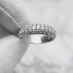 a white gold wedding band with round diamonds on it's side, sitting on top of a pillow