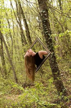 a woman in the woods is looking at herself in a mirror that hangs from a tree