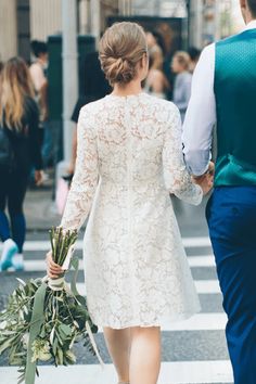 a man and woman walking down the street holding hands with flowers in each other's hand