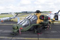 a helicopter sitting on top of an airport tarmac next to another plane with propellers