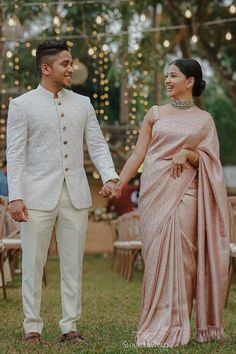 a man and woman holding hands while standing next to each other in front of string lights