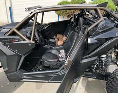 the side view of a black can - am commander with its doors open, parked in front of a garage