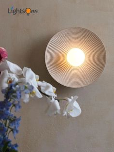 a light that is on the side of a wall with flowers in front of it