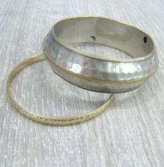 "A pair of matching Vintage brass bracelets in boho style, can be worn as a set or each one separately. These bracelets were a travel souvenir from India, made in the 1980s. Wide bracelet: silver plated brass, 14 mm wide and 6-7 mm thick with textured hammered surface and a rib around the middle. The silver plate is a bit worn off, the edges and the rib looks gold color. Narrow bracelet: 6 mm wide, gold plated brass with textured surface, the pattern looks like flowers and leaves. Length: 8 inch Hammered Silver Brass Bracelets, Silver Hammered Brass Bracelets, Bohemian Hammered Brass Bracelets, Hammered Metal Bangle, Bohemian Gold Hammered Bracelets, Festival Brass Bracelets In Silver Color, Silver Hammered Bohemian Bracelets, Silver Brass Bracelets For Festival, Bohemian Hammered Metal Bracelets