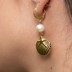 Get ready to shine with the Charleston Earrings! These gold-colored huggie earrings are pure coastal charm, featuring delicate pearl accents and adorable gold sea shell charms. Perfect for adding a touch of beachy elegance to any outfit, the Charleston Earrings will have you dreaming of sun-soaked shores and salty sea breezes. Whether you're out for a stroll by the beach or just wishing you were, these earrings bring a splash of ocean fun wherever you go. Slip them on and let the seaside magic b Gold Shell Drop Earrings, Ocean-inspired, Gold Ocean-inspired Shell Drop Earrings, Gold Pearl Charm Earrings For Beach, Gold Pearl Earrings For Beach, Gold Pearl Earrings With Charm For Beach, Gold Shell Earrings With Pearl Charm, Ocean-inspired Gold Pearl Earrings For Beach, Gold Dangle Shell Earrings Ocean-inspired, Summer Gold Shell-shaped Pearl Earrings