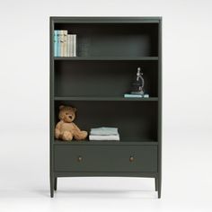 a teddy bear sitting on top of a green book shelf next to a white wall