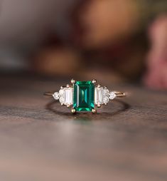 an emerald and diamond ring sitting on top of a wooden table