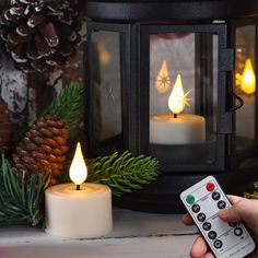 a person holding a remote control in front of a lit candle and pine cone decorations