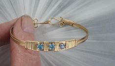 ELEGANT BLUE TOPAZ  GEMSTONE  BANGLE BRACELET IN 14KT ROLLED GOLD  HANDCRAFTED IN 14KT ROLLED GOLD IN A UNIQUELY DESIGNED SETTING 3  SWISS BLUE TOPAZ STONES 4mm UNIQUE HANDCRAFTED PIECE THAT WILL GET YOU NOTICED! LIGHTWEIGHT AND EASY TO WEAR SIZE ----- SIZE 6  TO 8 BRACELET IS 1/2 OF AN INCH WIDE ON THE SIDES iTS COMFORTABLE HEAVY DUTY HOOK AND CATCH MAKES IT EASY TO TAKE ON AND OFF AN EYE CATCHING PIECE! WEAR IT CASUAL OR FORMAL 7 THINGS TO KNOW ABOUT 14KT ROLLED GOLD #1. 14 Kt Rolled gold wire Sculpted Jewelry, Gemstone Bangle Bracelets, Wrap Bangles, Wire Wrapped Jewelry Tutorials, Gemstone Bangle, Blue Topaz Gemstone, Blue Topaz Stone, Bracelet Gemstone, Bracelet Cuff