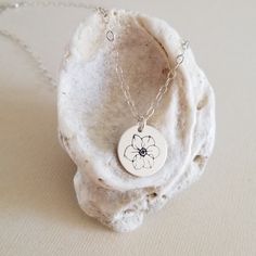 a necklace with a flower on it sitting on top of a white piece of rock