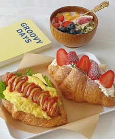 two croissants with strawberries on them are next to a bowl of fruit