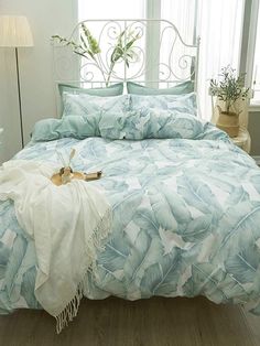 a bed with blue and white comforter next to a plant in a vase on the floor