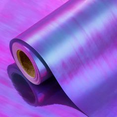 a roll of purple metallic foil sitting on top of a pink tablecloth with a shadow