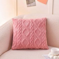 a pink pillow sitting on top of a white couch next to a cup and saucer