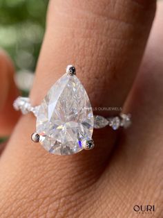 a woman's hand holding an engagement ring with a pear shaped diamond on it