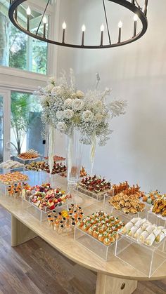 a table topped with lots of desserts on top of a wooden table next to a chandelier