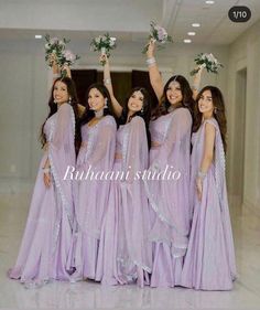 the bridesmaids are dressed in lavender colored saris and holding flowers up to their heads