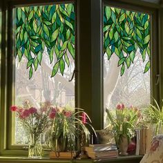 two windows with green leaves on them and flowers in vases next to each other