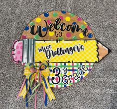 a welcome sign is on the ground with some ribbon around it's neck and two pencils in front of it