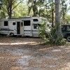 an rv is parked in the woods next to some trees and two other vehicles are parked behind it