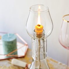 a lit candle in a clear glass vase on a table with other items around it