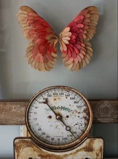 an old clock with wings on it sitting next to a wall mounted thermometer