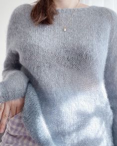 a woman wearing a gray sweater is holding her hand in her pocket and looking at the camera