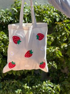 This strawberry tote bag with flowers is fun, lightweight, and is the perfect eco friendly reusable grocery tote bag. The strawberries add beautiful bright color, fun, and a cute aesthetic to go with your outfits. Use you tote bag in place of a purse, to carry your laptop, water bottle or other goodies.  This canvas tote is natural color and is 100% cotton.  Strawberry pattern may differ slightly as they are hand placed. CARE INSTRUCTIONS: Wash inside out on a gentle cycle. Hang dry. Iron inside out. Do not iron directly on top of the design.  Please message us with any questions.  Thank you! Painted Totes Ideas, Tote Bag Pattern Paint, Flower Tote Bag Painting, Cute Spring Tote Bag, Cute Strawberry Print Tote Bag, Summer Strawberry Print Bag For Daily Use, Summer Strawberry Print Bags For Daily Use, Cute Reusable Tote Bag, Tote Bag Design Ideas Paint