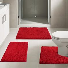 three red rugs sit in front of a white toilet