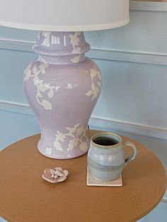 a table with a vase and a cup on it, next to a lamp shade