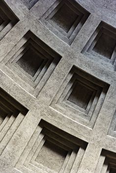 black and white photograph of an abstract concrete structure with square openings in the center, viewed from below