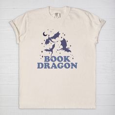 Immerse yourself into a fantasy world with our Book Dragon Comfort Colors T-Shirt. Blend your passion for dragons and love for books with this comfy cotton tee. The design features a stylish 'Book Dragon' catchphrase that echoes your identity as a fantasy reader in a fun way. This T-shirt is made from 100% ringspun cotton, offering a vintage feel and ultimate comfort, making it your perfect companion for reading marathons or casual day outs. Each book dragon shirt is lovingly crafted, promising longevity and consistent comfort. Stand out and wear your love for books and dragons with this unique shirt! Experience cozy reading bliss every day in a Comfort Colors 1717 unisex tee. Revel in the luxurious feel of 100% USA grown, ring-spun cotton and enjoy a garment that's been washed to peak sof Literary Crew Neck T-shirt With Screen Print, Screen Print Crew Neck T-shirt, Relaxed Fit Pre-shrunk Bookish T-shirt, Literary Graphic Print Crew Neck T-shirt, Literary Cotton Relaxed Fit T-shirt, Literary Style Cotton T-shirt With Relaxed Fit, Bookish Cotton T-shirt With Slogan, Literary Cotton T-shirt With Text Print, Bookish Crew Neck T-shirt With Graphic Print