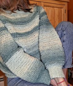 a woman sitting on the floor with her legs crossed and wearing a sweater that is crocheted