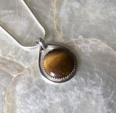 This petite pendant features a lovely, natural, Tiger's eye gemstone. I chose this gemstone because I have always been drawn to its energy and had yet to work with it!  I loved the movement in the stone, and wanted to keep the setting simple but unique. I started with a pure silver, serrated, bezel wire, to secure the stone. Then I created a sterling silver platform to reveal the back of the stone, while securing it. Then, I created a pear shape with think sterling silver wire. I placed the Tiger eye inside, and soldered it to the bottom right side of the shape. I used a lined and dimpled pattern on the bale to add texture and reinforce the modern look.  The bale is about 5mm, allowing for a variety of chains to comfortably be threaded through!  Since I was a child, I have been drawn to Ti Bezel Wire, Eye Meaning, Silver Platforms, Tiger Eye Gemstone, Tiger Eye Crystal, Tigers Eye Necklace, Tigers Eye Gemstone, The Tiger, Tiger's Eye