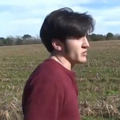 a man in a red shirt standing in the middle of a field looking at something