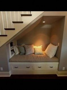 a room with some drawers under the stairs and a bench underneath it that has pillows on it