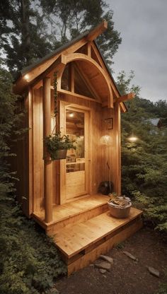 a small wooden cabin in the woods with lights on and potted plants growing inside