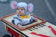 a baby in a mouse costume sitting on top of a wooden cart with metal bars