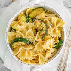 pasta with zucchini and spinach in a white bowl on top of a napkin